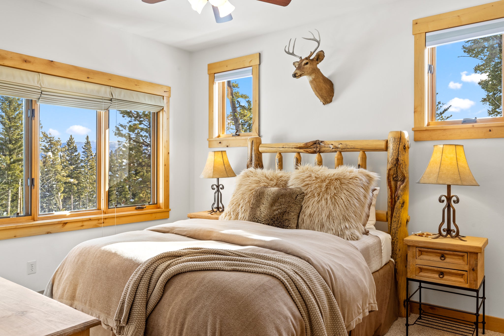 Queen size bed on log bed frame with plush pillows beneath a deer bust mount in Big Sky, Montana
