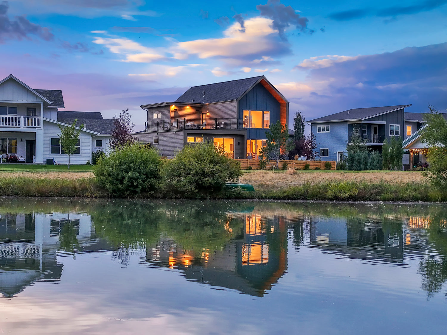 Exterior listing photo taken at twilight of lakefront home with water reflection and glowing windows in Bozeman, Montana