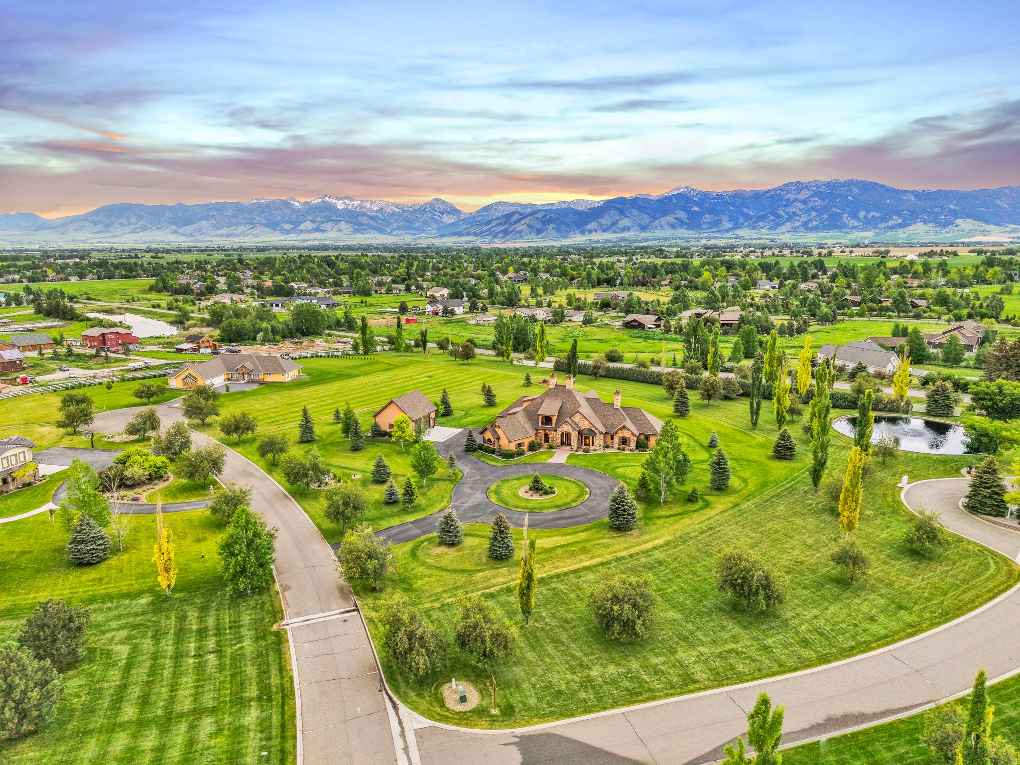 Aerial view of a suburban neighborhood with a large house in the center, surrounded by greenery and Bridger mountains in Bozeman, Montana