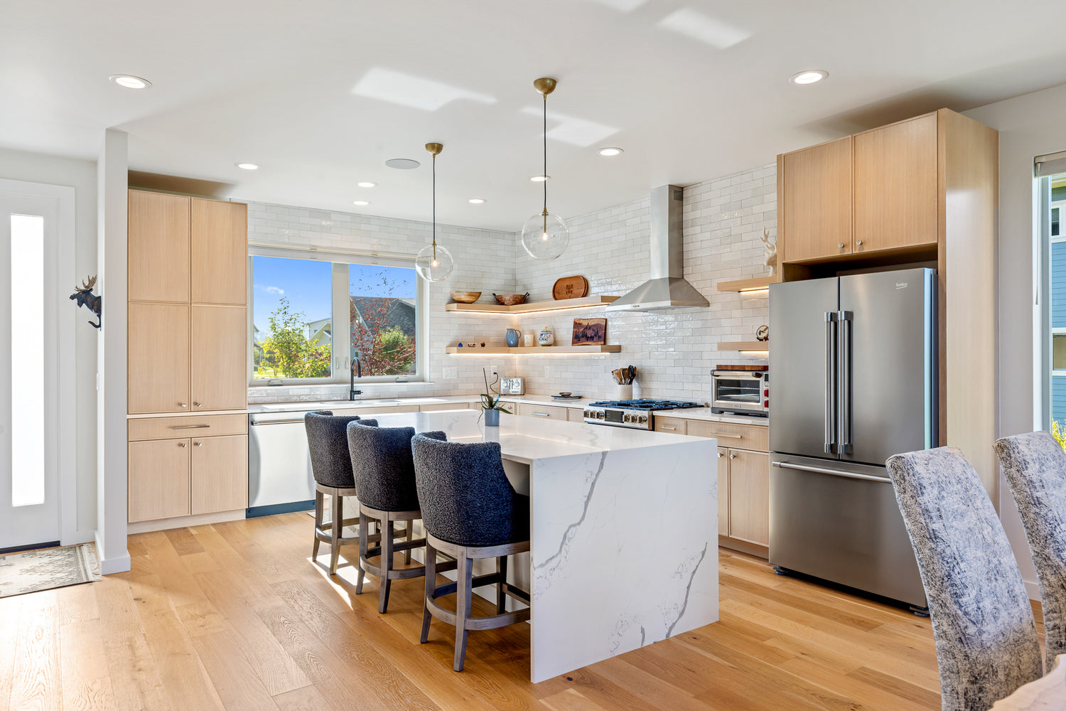 Bright kitchen with white marble counters, stainless appliances, and white subway tile walls with oak cabinets in Bozeman, Montana
